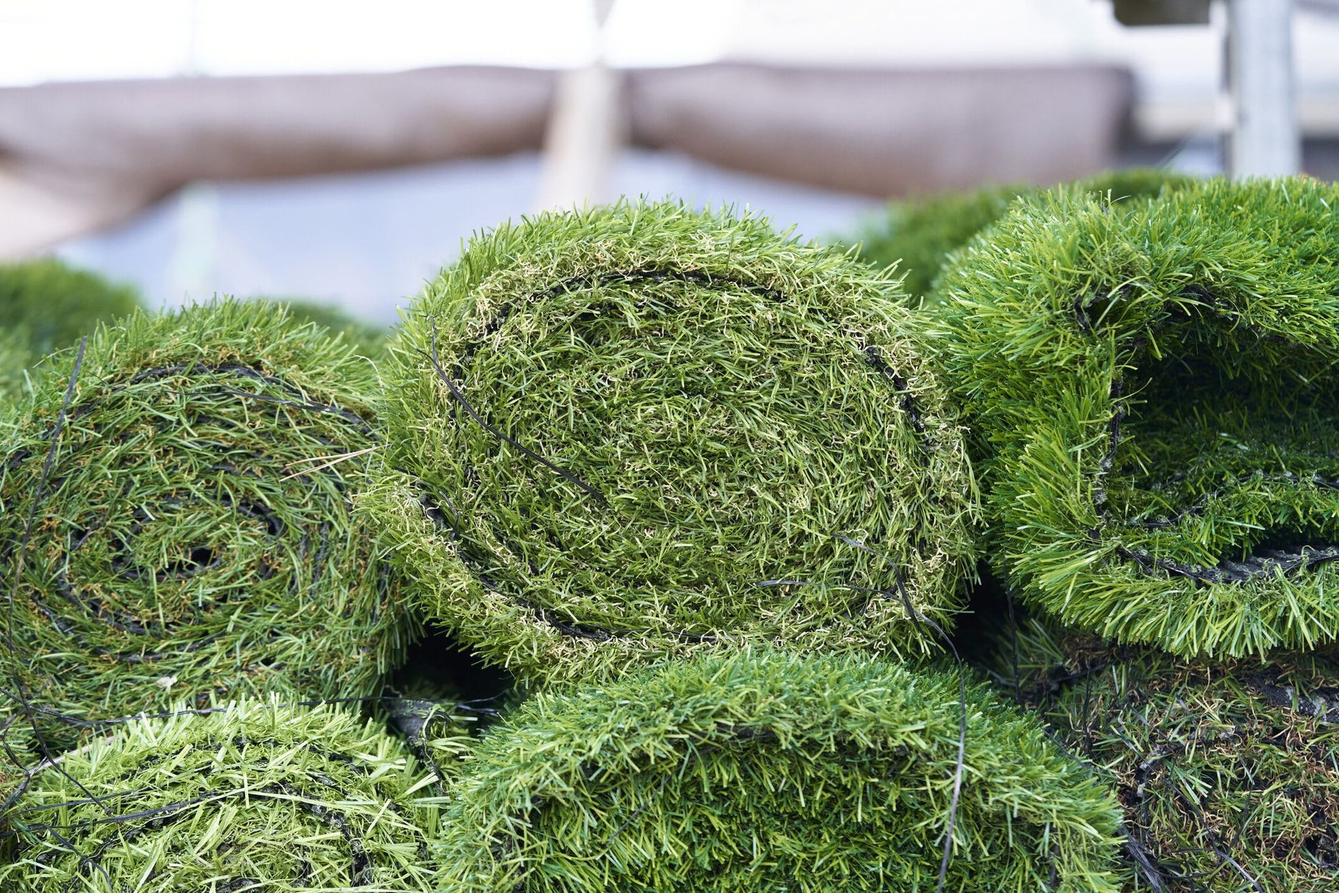 Tightly rolled grass turf stacked together in an outdoor or warehouse setting.