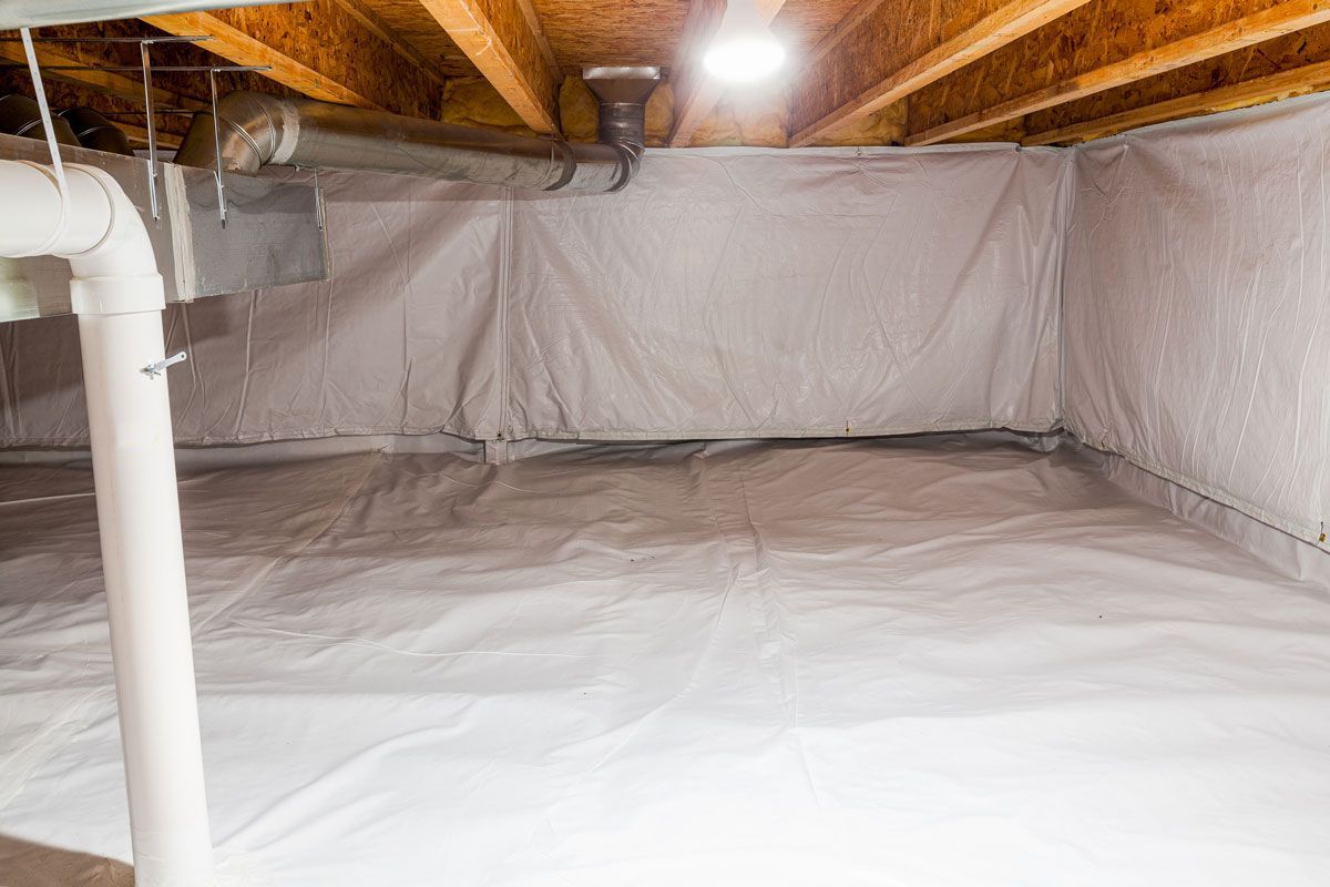 Interior of a crawl space covered in white vapor barrier; pipes and wooden beams visible.