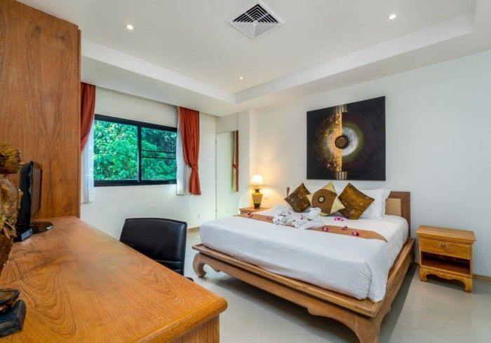 Bedroom with a wooden bed frame, desk, and abstract art, with white walls and a window.
