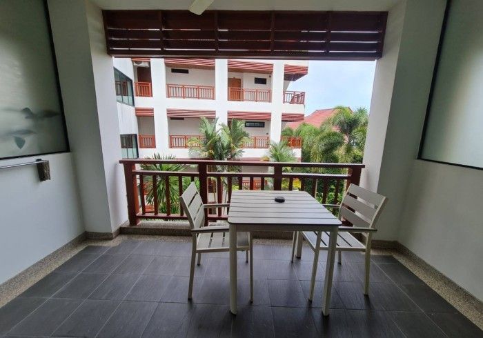 Balcony with white table and chairs, overlooking a building and trees.