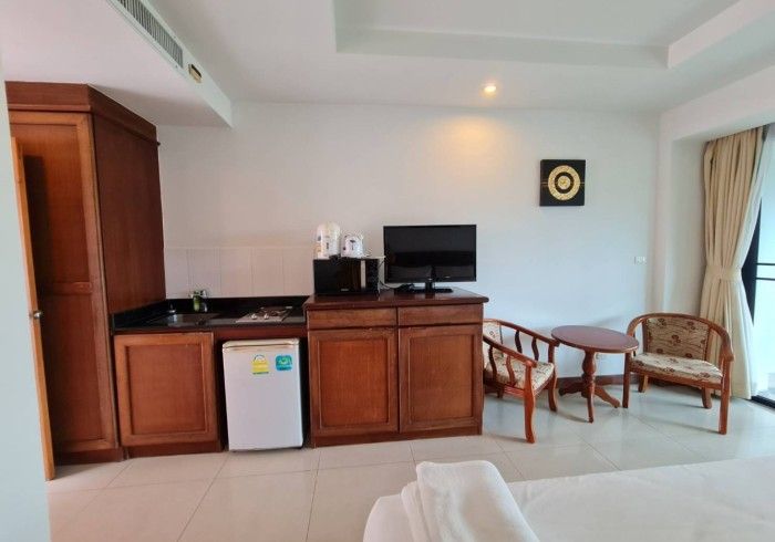 Hotel room interior: mini-kitchen with mini-fridge, microwave, TV, chairs, small table, and a bed.