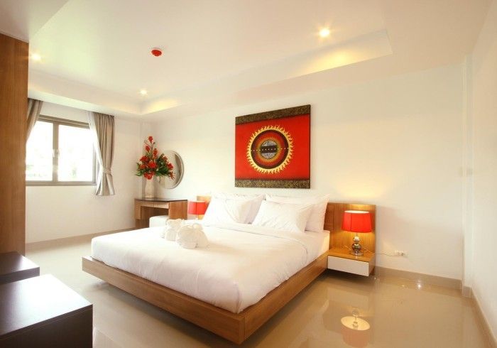 Bright hotel bedroom with king bed, art, red lamps, window, and wood furniture.