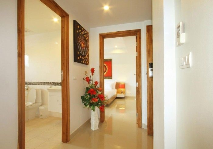 Hallway with open doorways to bathroom and bedroom, bright white walls, wooden door frames, art, and a vase of flowers.