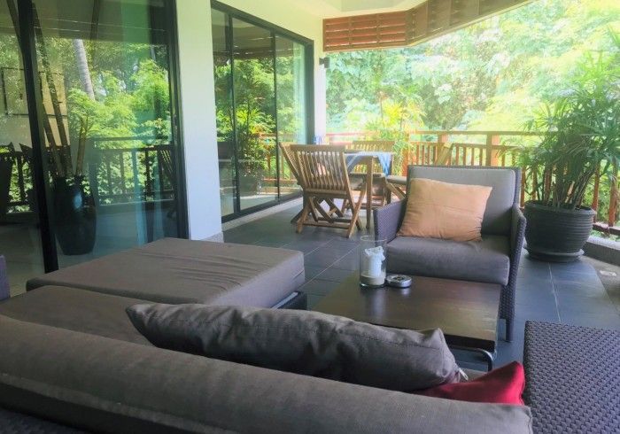 Outdoor patio with gray furniture, a small table, and lush greenery in the background.
