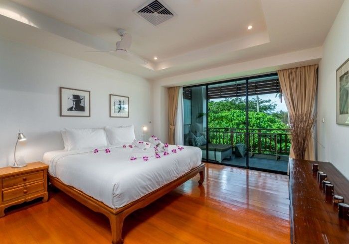 Bedroom with a king bed, hardwood floors, balcony with greenery view, and decorative flowers on the bed.