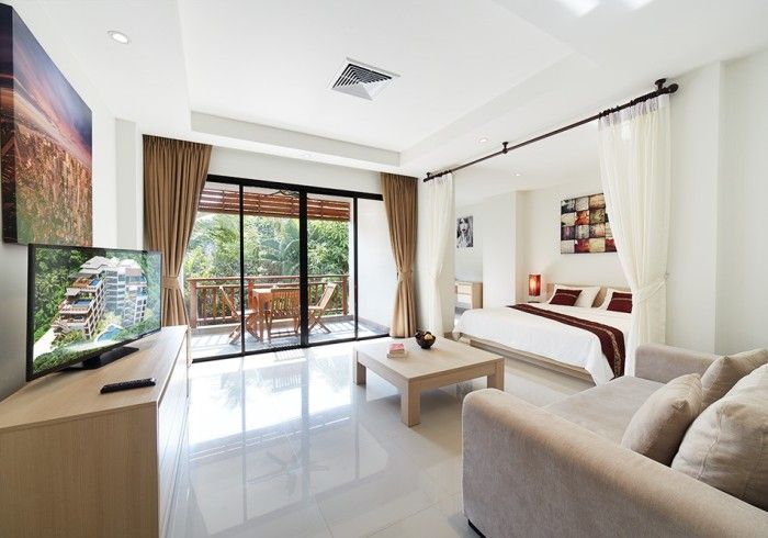 Modern hotel room with balcony access. Features a bed, couch, TV, coffee table, and sliding glass doors.