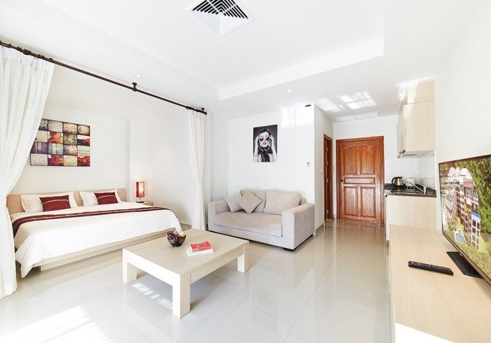 Bright studio apartment with white walls, a bed, a sofa, and a TV.