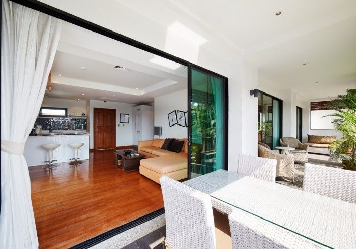 Patio dining area opens to a living room with tan couch and kitchen. Sliding glass doors and white curtains.