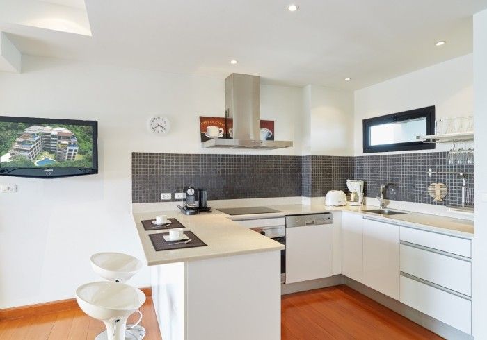 Modern kitchen with white cabinets, breakfast bar, stainless steel appliances, and a TV.