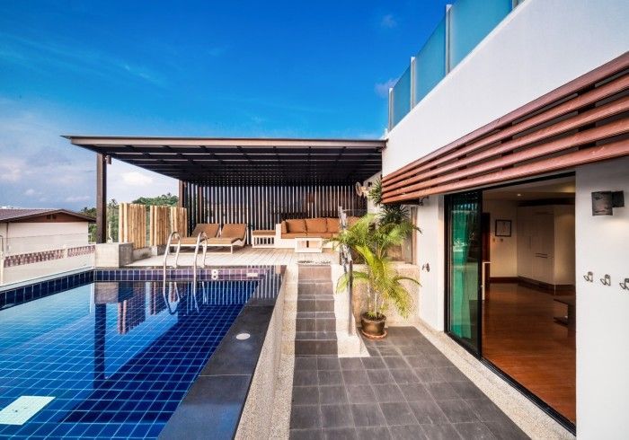 Rooftop pool and patio with seating area under a pergola. Blue sky overhead.