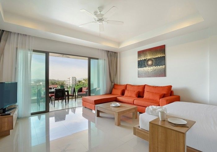 Living room with orange sectional sofa, balcony, and city view.