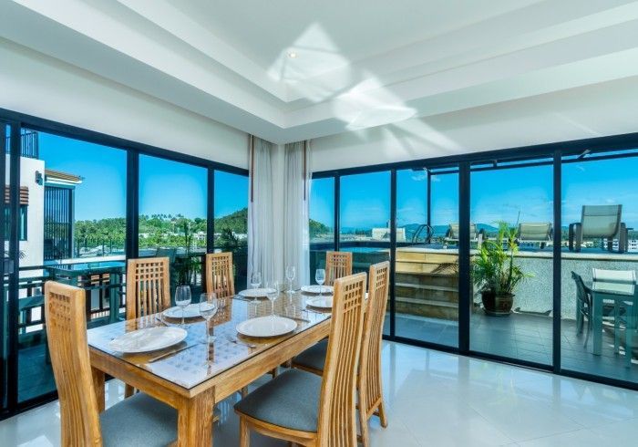 Dining room with a wooden table set for a meal, overlooking a balcony and blue sky.