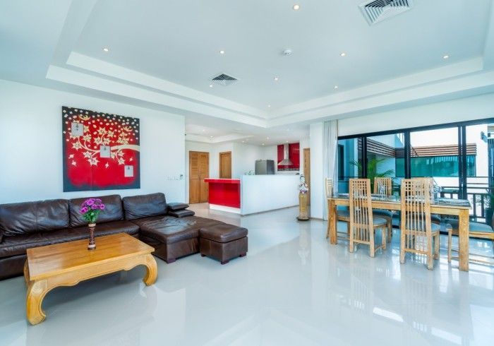 Spacious, modern living room with leather sectional, artwork, and dining area with bright red accent colors.
