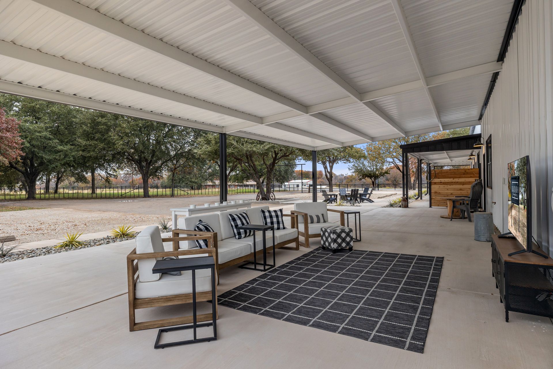 A covered patio with a couch , chairs , tables and a television.
