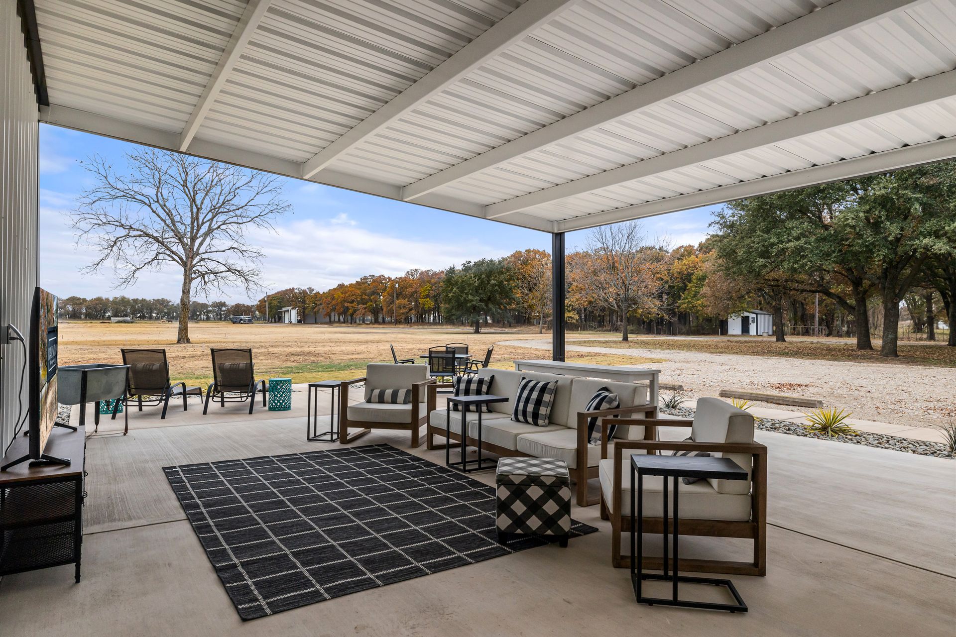 A covered patio with a couch , chairs , tables and a rug.