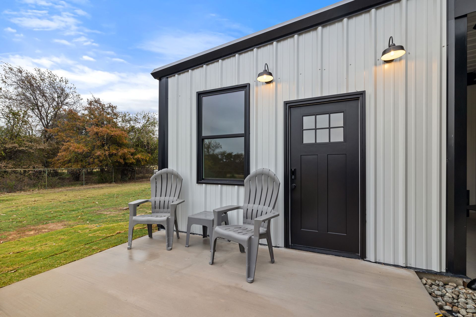 There are two chairs and a table on the patio in front of the house.