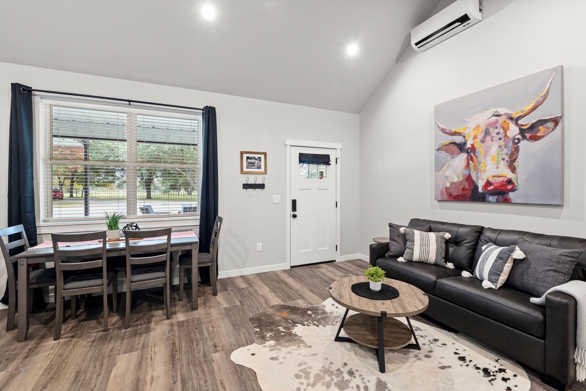 A living room with a couch , table , chairs and a painting of a cow on the wall.