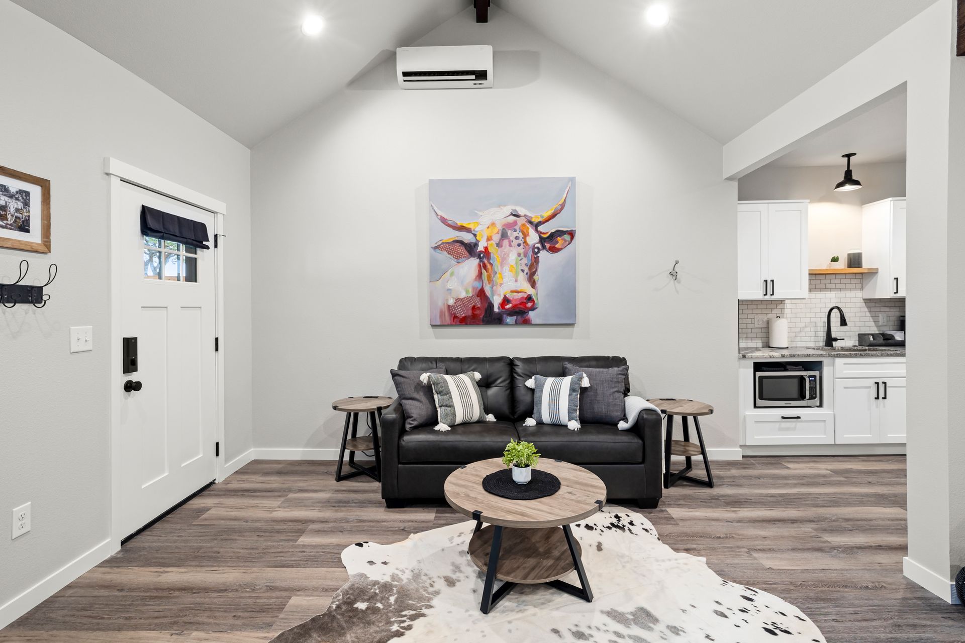A living room with a couch , coffee table , and a painting of a cow on the wall.