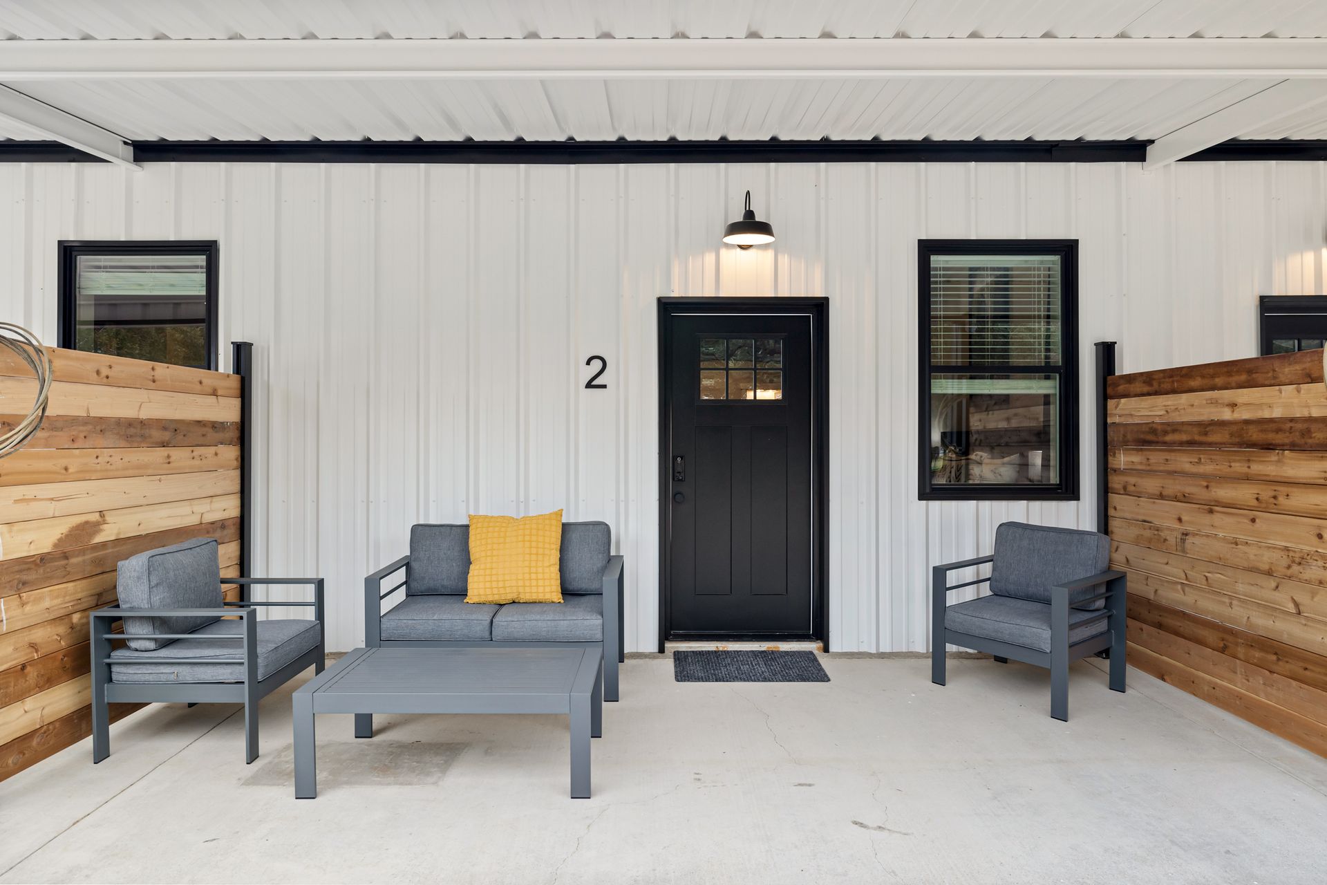 A patio with a couch and chairs in front of a house with the number 2 on the door.