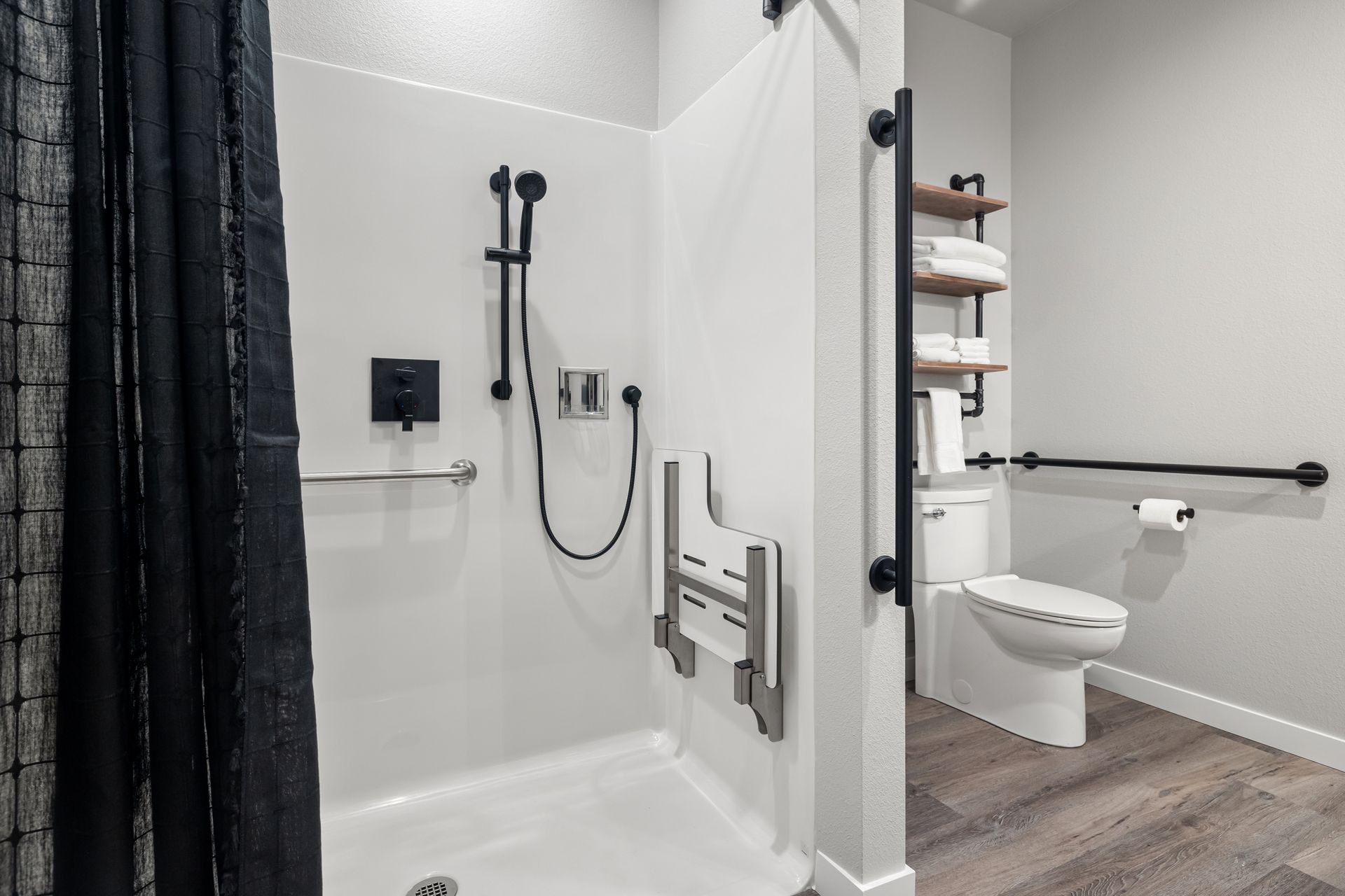 A bathroom with a shower , toilet , and handrails.