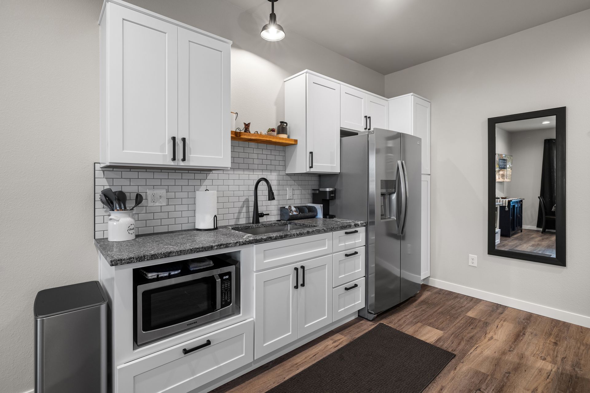 A kitchen with white cabinets , a stainless steel refrigerator , a microwave , and a mirror.