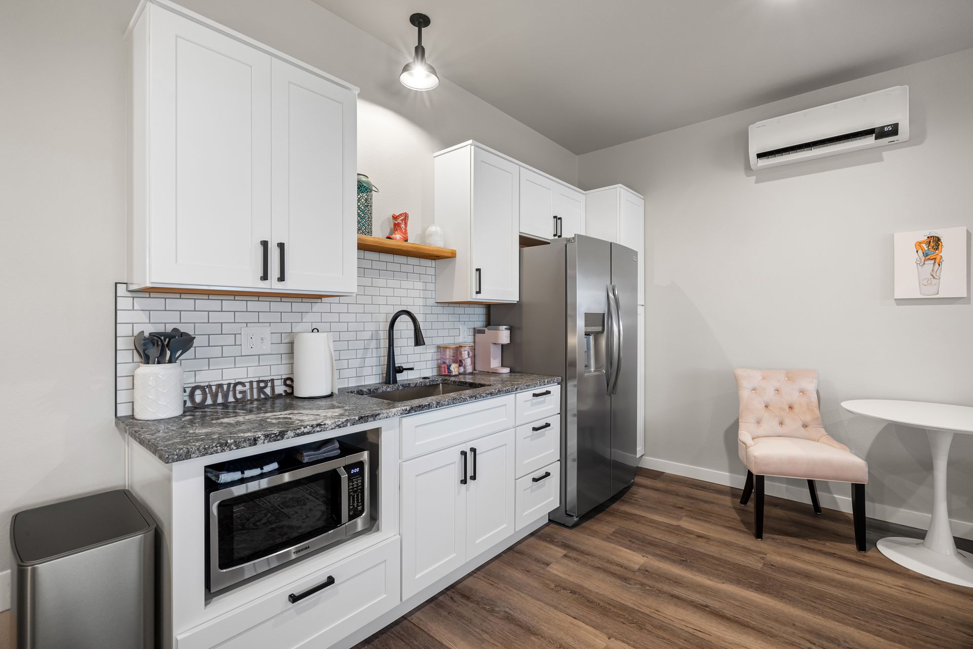 A kitchen with white cabinets , stainless steel appliances , a microwave , refrigerator , sink and chair.