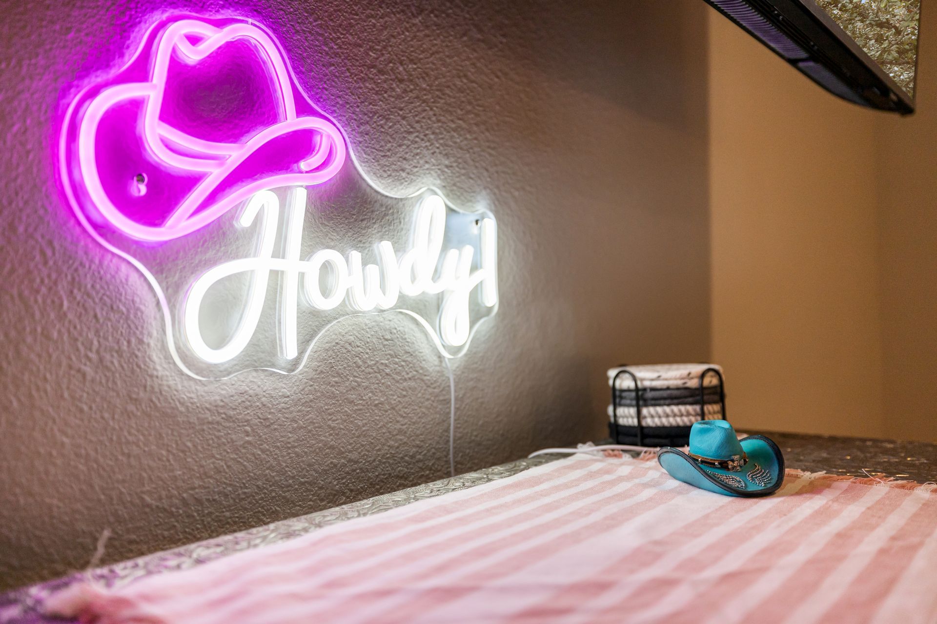 A neon sign with a cowboy hat on it is hanging on a wall next to a bed.