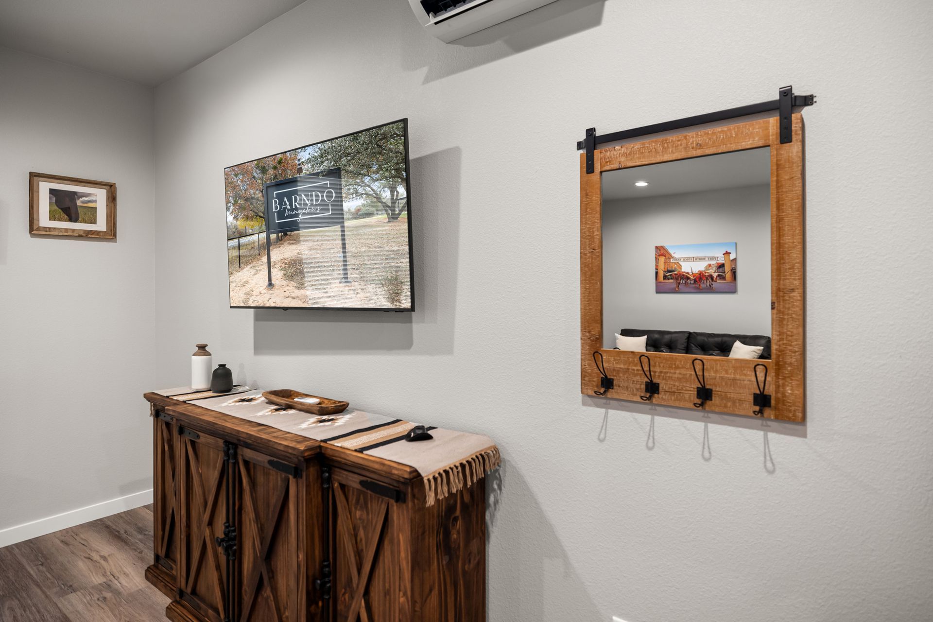 A living room with a wooden dresser , a flat screen tv , and a mirror.