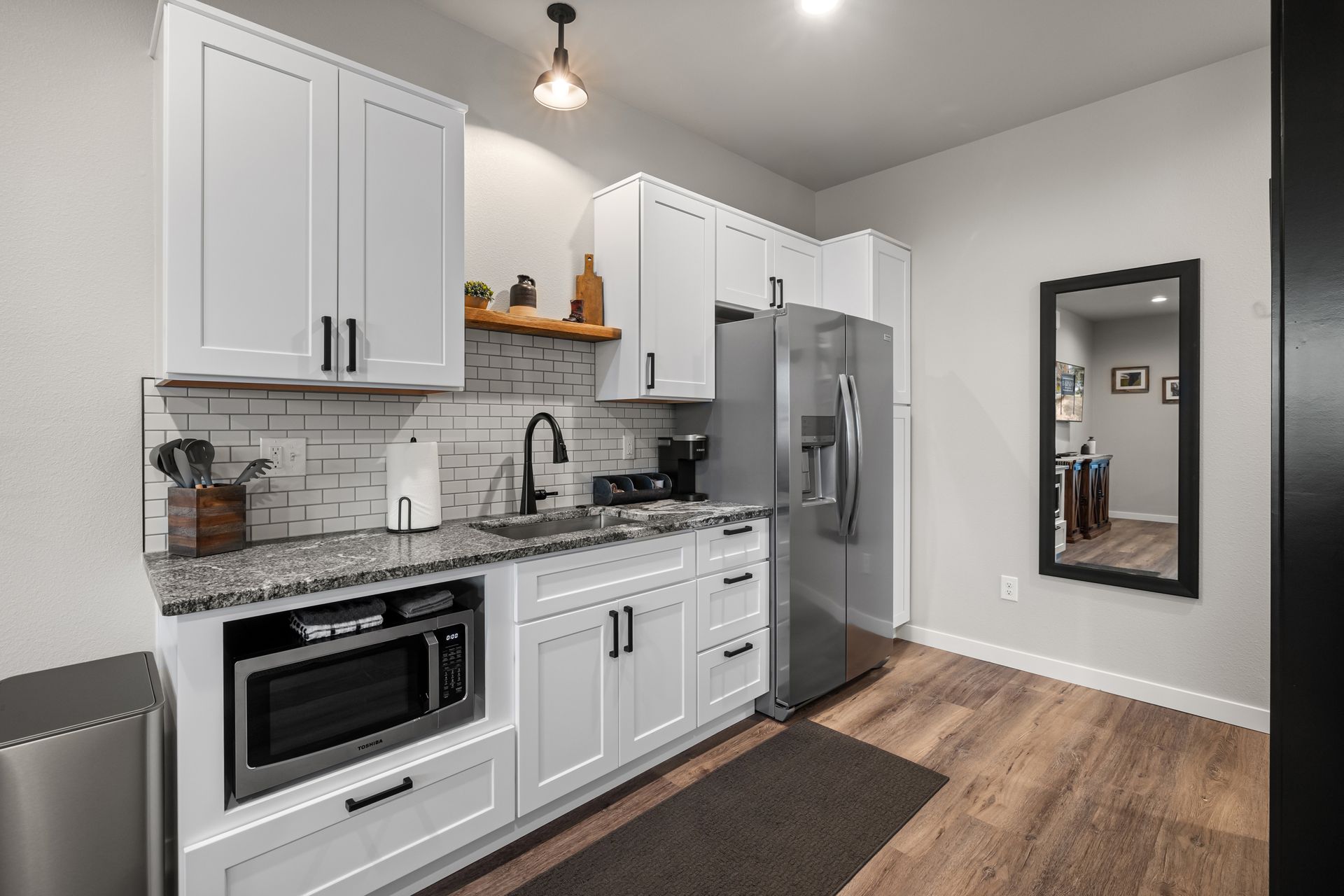 A kitchen with white cabinets , stainless steel appliances , a microwave , refrigerator , sink and mirror.