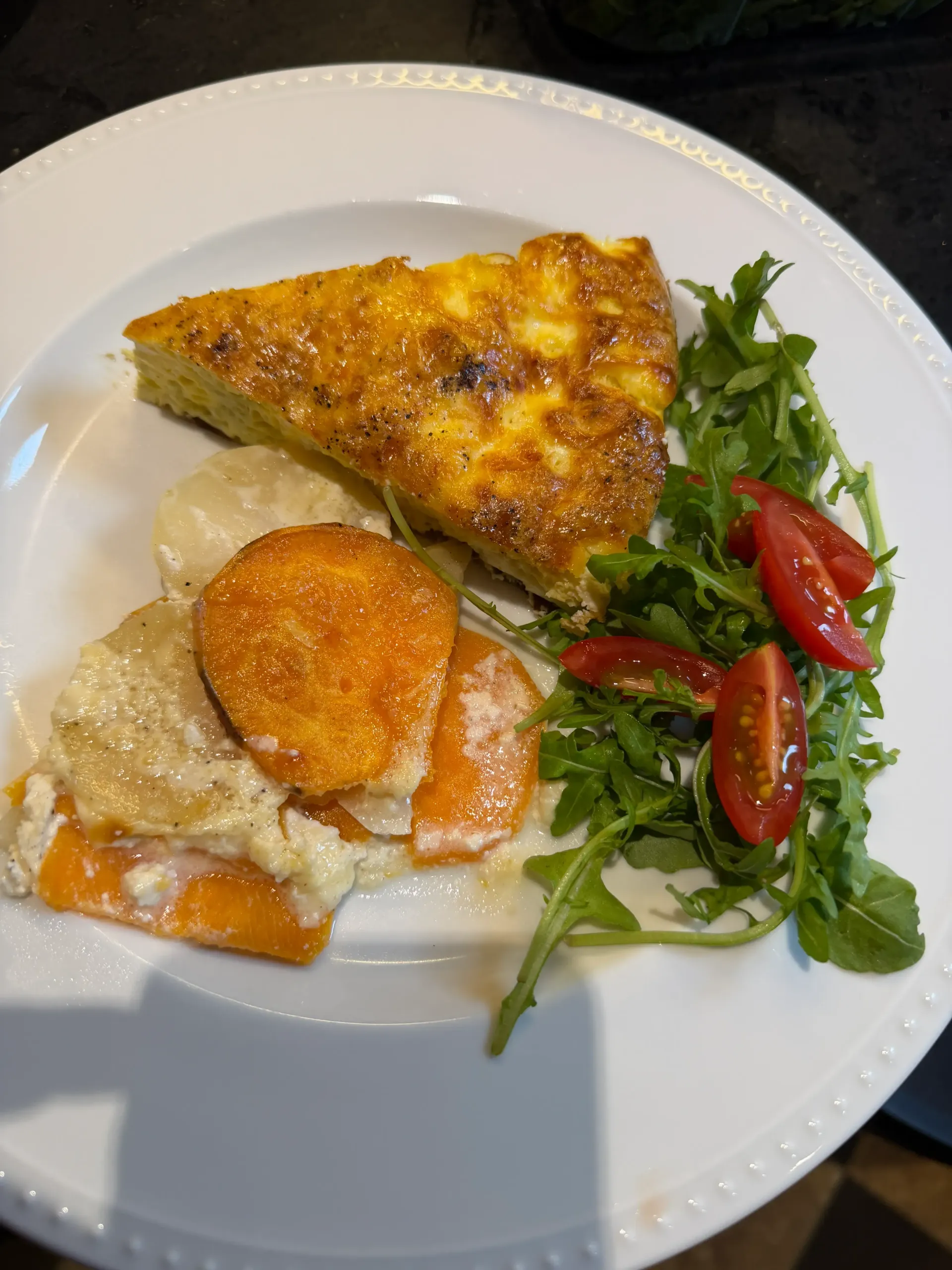 Plate of food: quiche, sweet potatoes with creamy sauce, arugula, and halved cherry tomatoes.