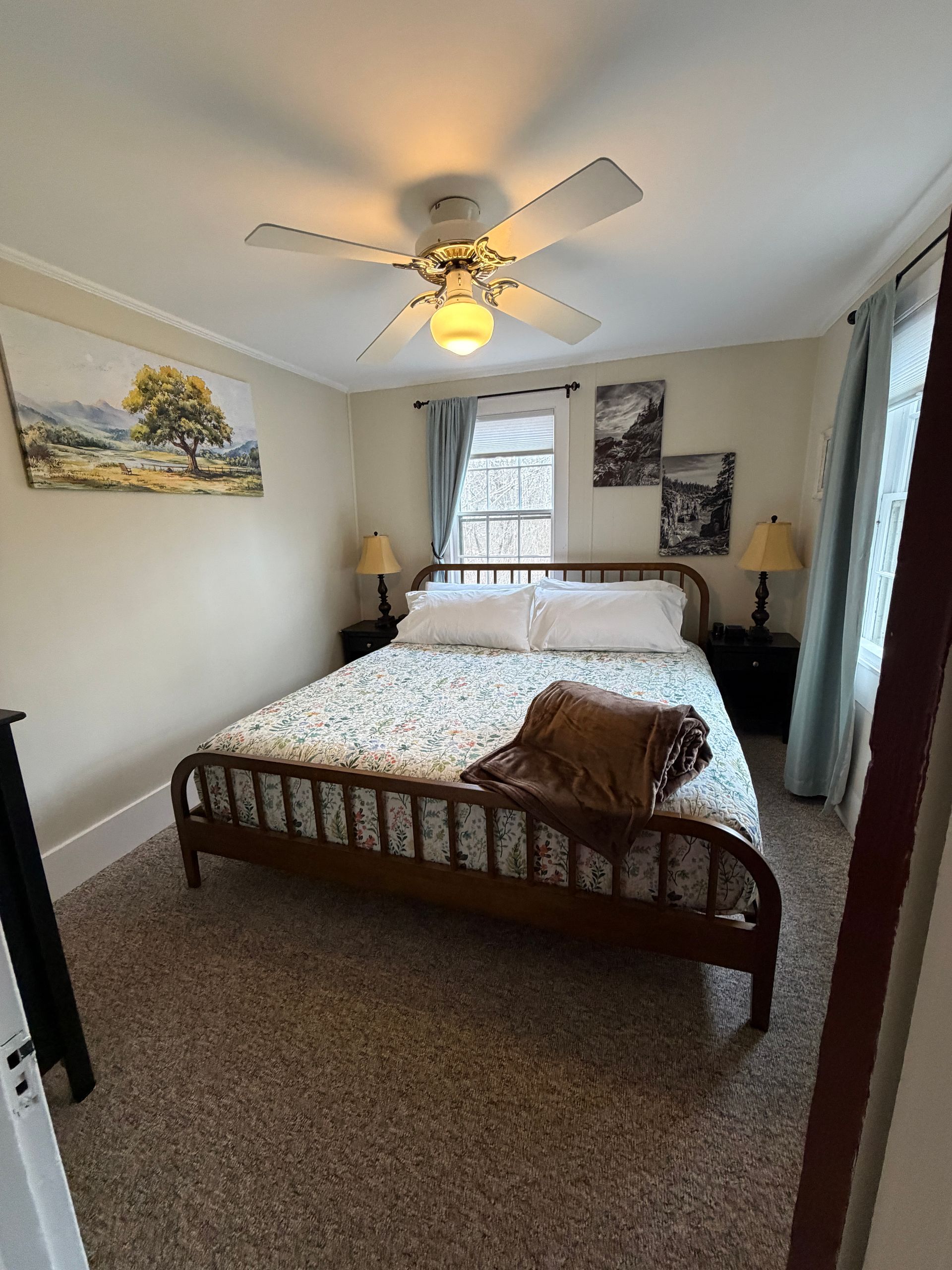 Small bedroom with a wooden bed, patterned bedding, ceiling fan, and two bedside lamps.