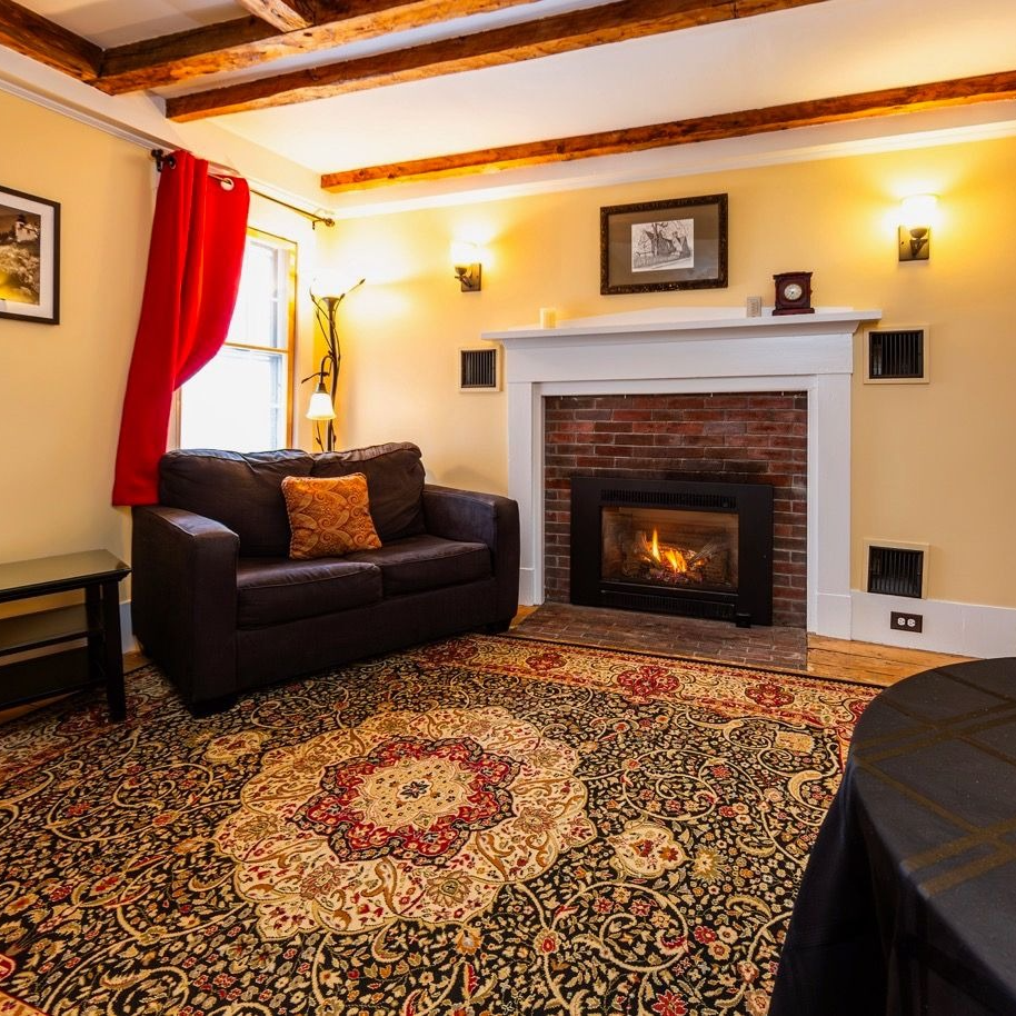 Cozy living room with fireplace, brown sofa, red curtain, and patterned rug.