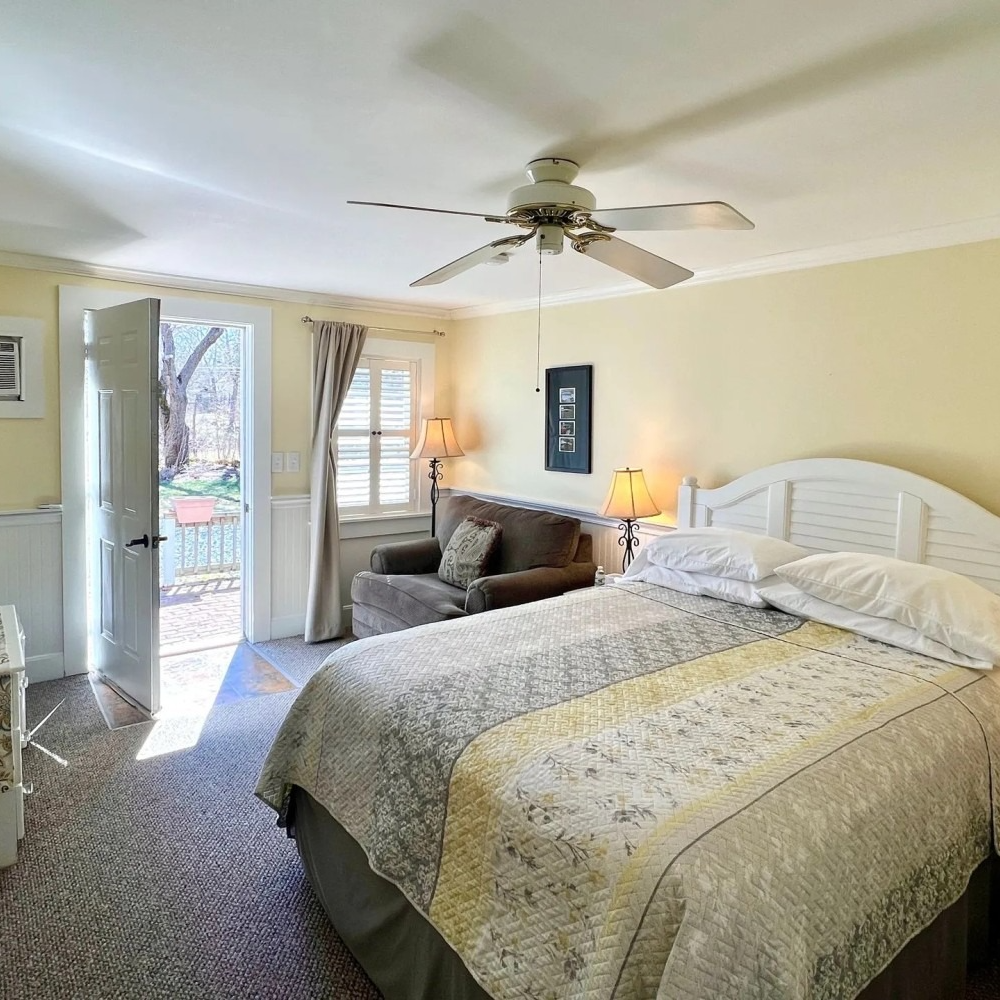 Bedroom with a queen bed, loveseat, and door to a patio. Beige walls, neutral colors.