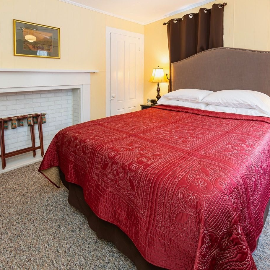 Bedroom with a red bedspread, fireplace, and luggage rack.