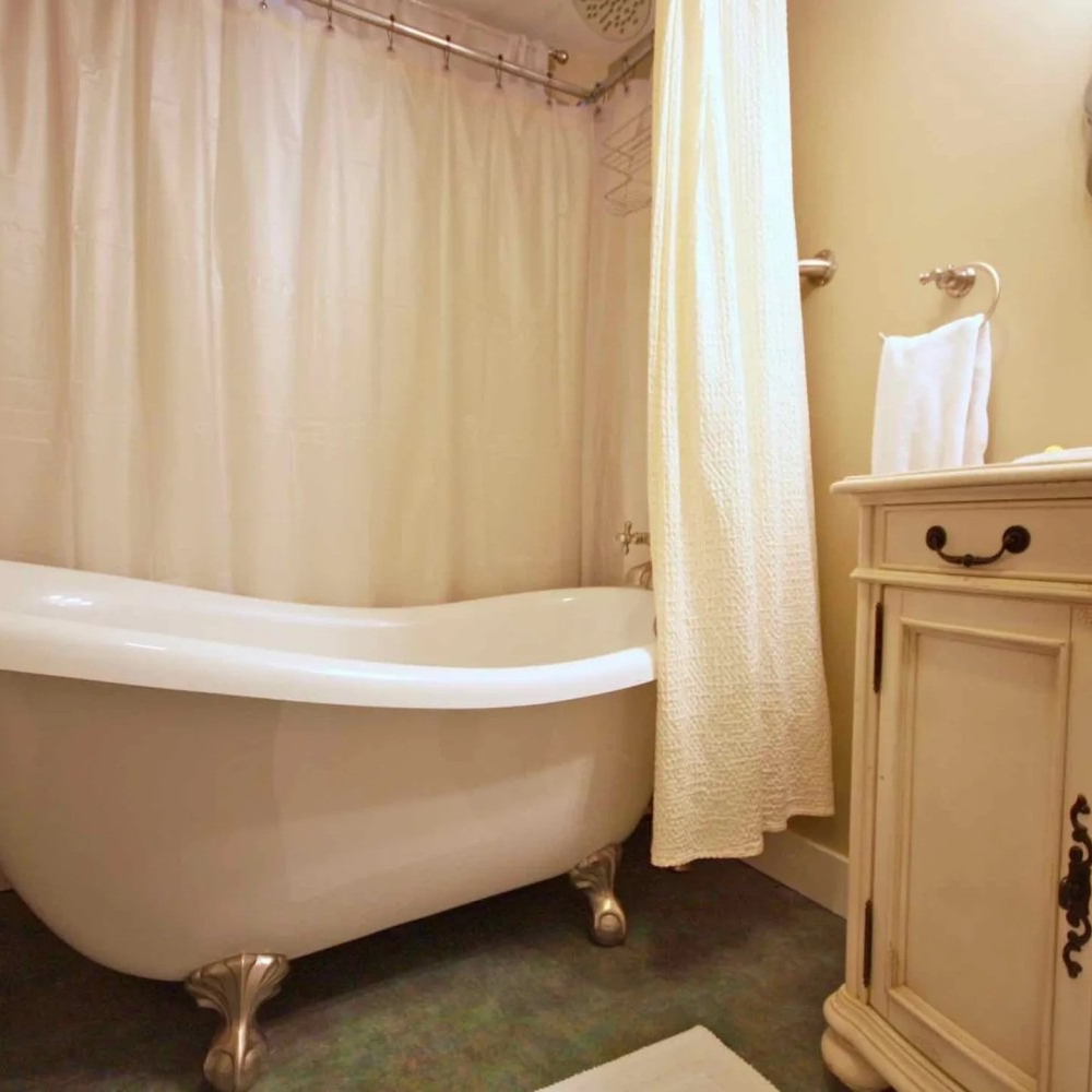 Claw-foot bathtub with a white shower curtain and matching cabinet in a bathroom.