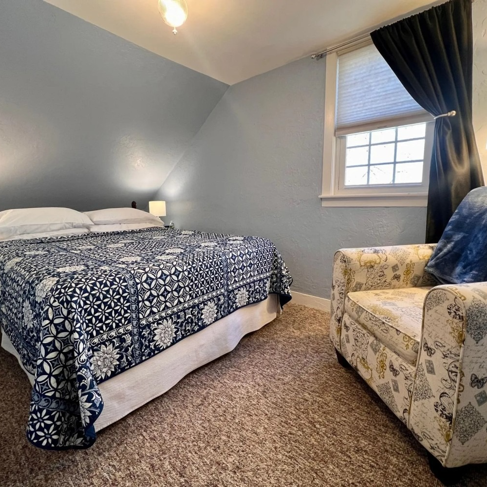 Bedroom with a bed, armchair, window with blinds, and blue walls.