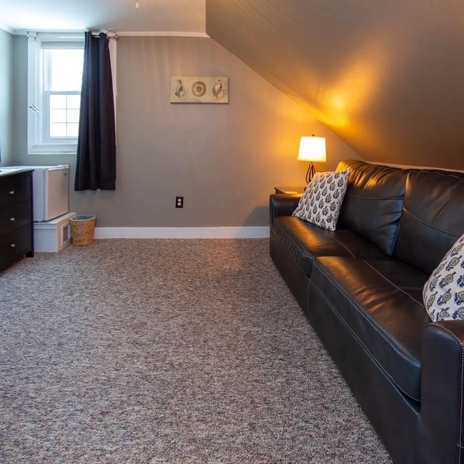 Cozy attic room with black leather sofa, desk, window, and neutral-colored carpet.