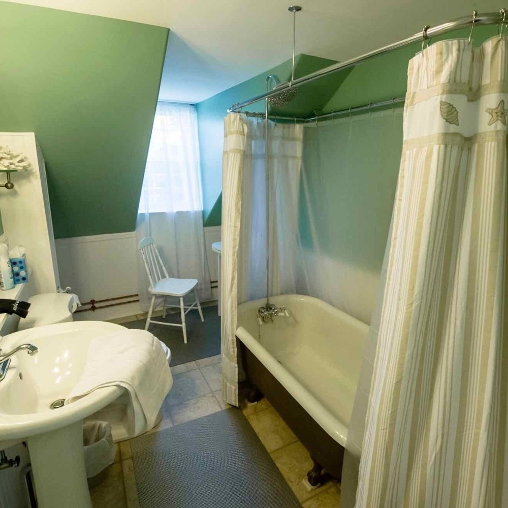 Bathroom with clawfoot tub, pedestal sink, and green walls. Beige striped shower curtain.