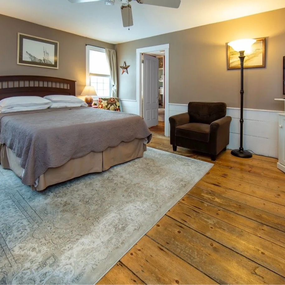 Bedroom with a bed, chair, lamp, rug, and wooden floors.