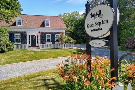 Coach Shop Inn sign in front of a white trimmed house with flowers and a gravel driveway.