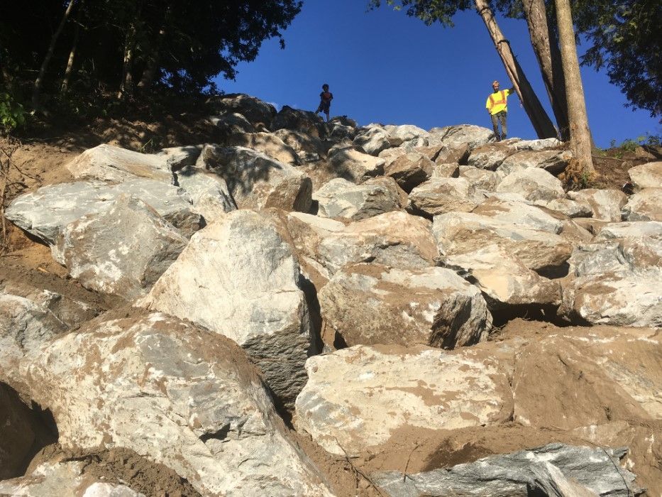 Un homme en veste jaune se tient au sommet d'une colline rocheuse.