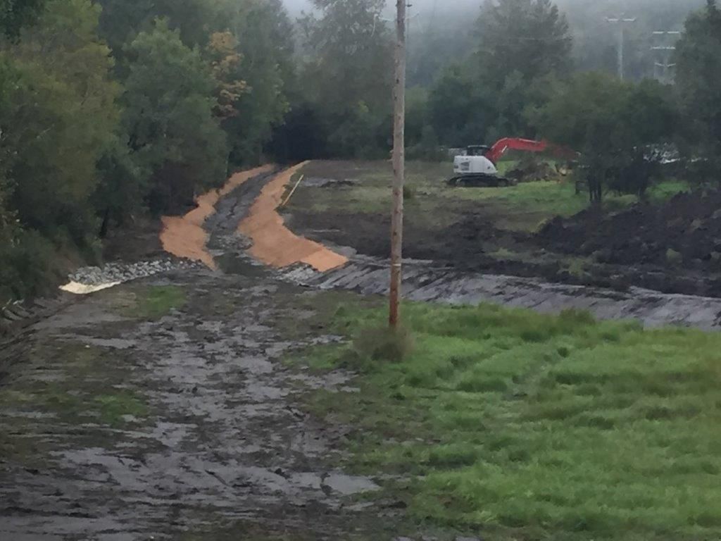 Une route boueuse traversant un champ herbeux avec des arbres en arrière-plan.