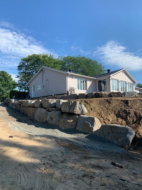 Une maison est située au sommet d'une colline de terre, à côté d'une paroi rocheuse.