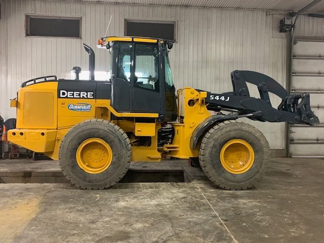 Une chargeuse sur pneus Deere jaune est garée dans un garage.