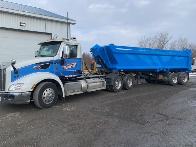 Un camion-benne avec une remorque bleue est garé devant un immeuble.
