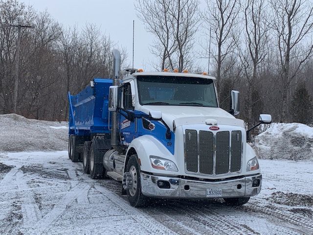 Un camion à benne basculante roule sur une route enneigée.