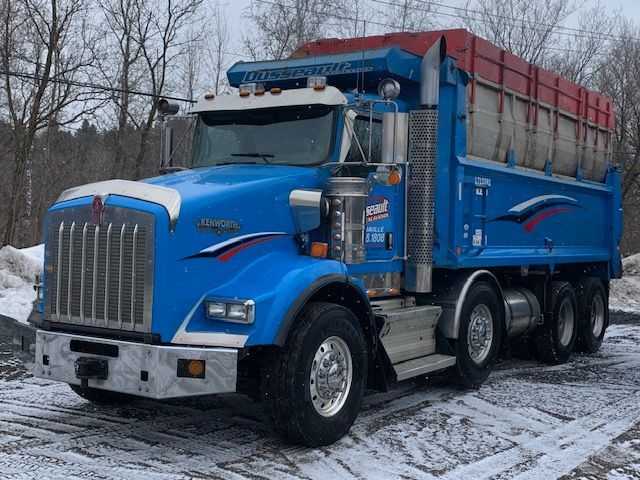 Un camion à benne bleu est garé dans la neige.