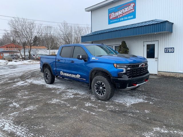 Un camion bleu est garé devant un bâtiment dans la neige.