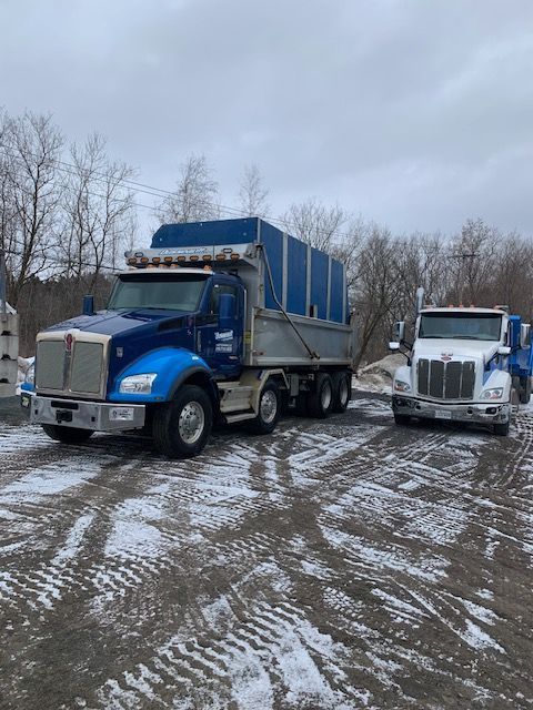 Deux camions à benne basculante sont garés dans un terrain enneigé.