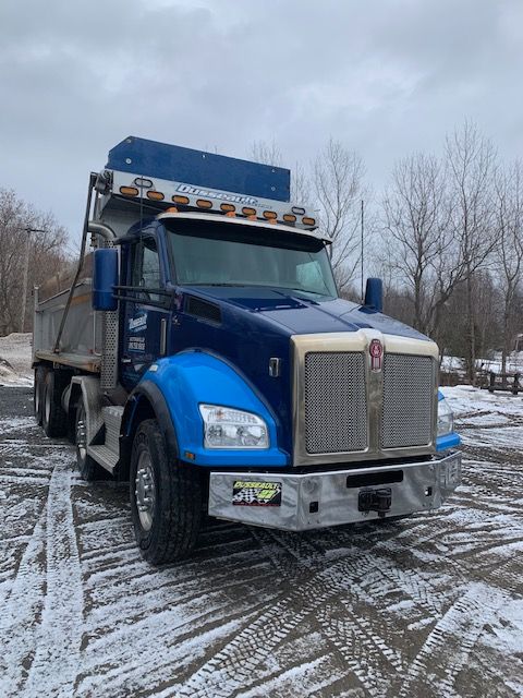 Un camion-benne bleu est garé dans un parking enneigé.